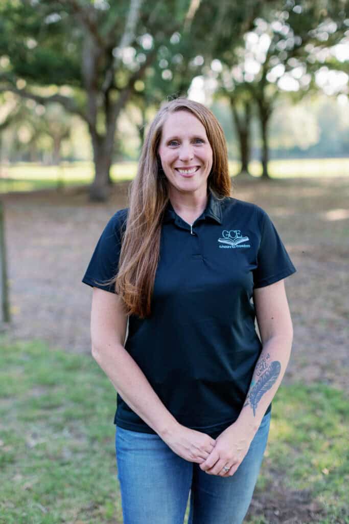 A woman in a GCE polo shirt standing outdoors with trees in the background, representing a classical Christian homeschool pro.