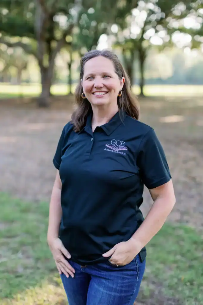 A woman smiling outdoors in a navy polo with GCE logo, representing classical Christian homeschooling.