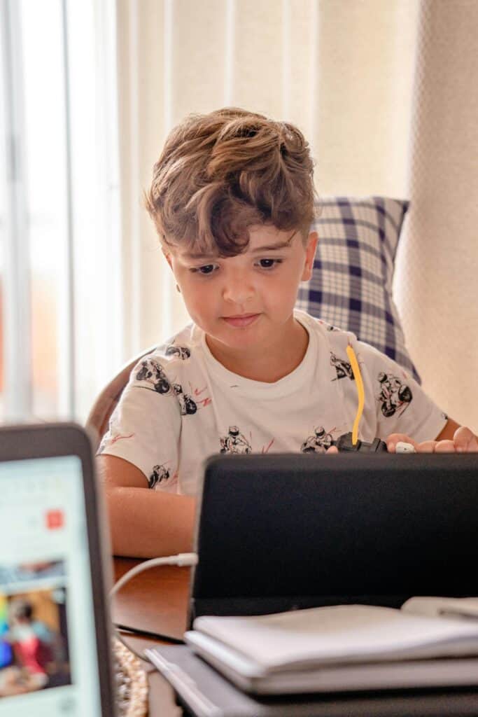 Young boy studying with tablet and books at home, engaged in online hybrid learning for elementary education.