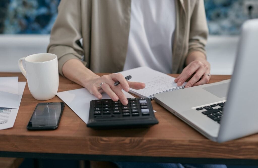 Parent at a table with a notebook, laptop and calculator working out online classical homeschool cost