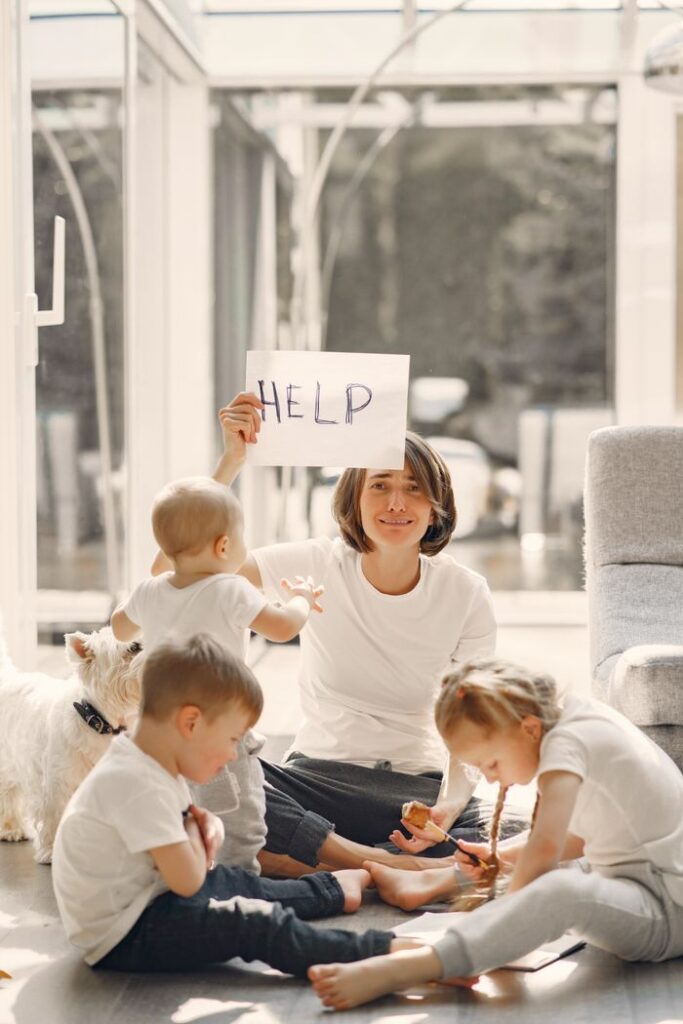 pexels-photo-4017419-4017419 Woman holding placard with sign help while looking after children on floor in well lit living room